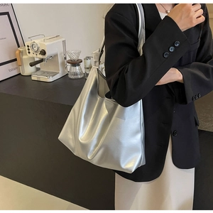 Silver metallic tote bag with knot strap detail worn by model in a cafe setting