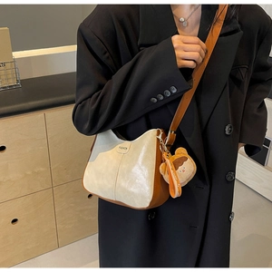 Détail d'un sac bandoulière demi-lune bicolore avec un ours en peluche et étiquette fashion
