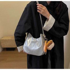 Détail d'un sac bandoulière argenté mat avec logo de mode et breloque en peluche