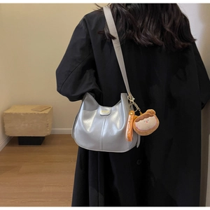 Detail of silver faux leather shoulder bag with plush charm and gold brand plate