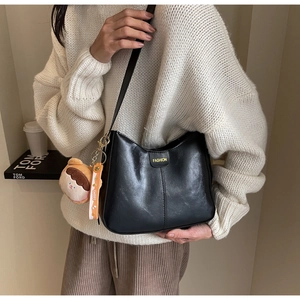 Détail d'un sac bandoulière en cuir noir avec texte mode et pendentif en peluche mignon