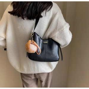 Vue arrière d'un sac bandoulière demi-lune noir avec un pendentif peluche sur un pull en maille