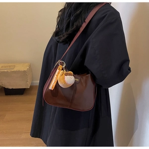Détail d'un sac bandoulière marron en demi-lune avec peluche et ruban imprimé