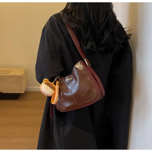 Détail du sac bandoulière en cuir marron foncé avec breloque ours et large bandoulière bordeaux