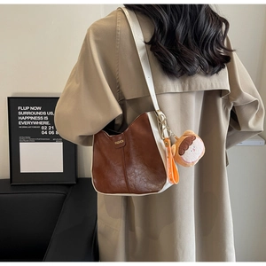 Détail du sac hobo en cuir marron et blanc avec un porte-clés peluche et tag Fashion