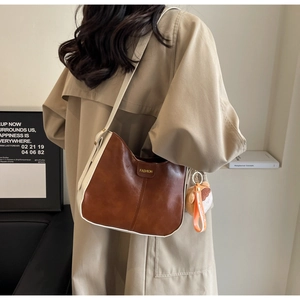 Gros plan d'un sac bandoulière bicolore marron et beige avec un pendentif mignon