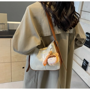 Détail du sac hobo crème avec bordure marron et charmant pendentif peluche sur le modèle