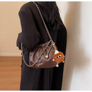 Detail of brown pleated dumpling bag with gold chain strap and fuzzy monster charm