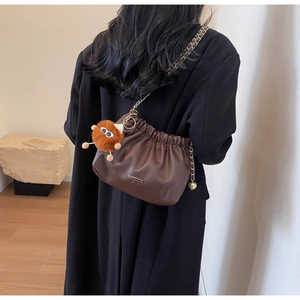 Detail of soft brown leather bucket bag featuring chain strap and plush monster charm