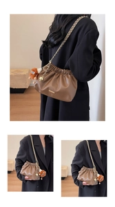 Detail of brown pleated cloud bag with chunky gold chain and cute plush monster charm