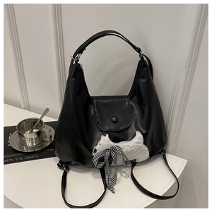 Detail der schwarzen Hobo-Tasche mit weißem Plüschwelpen und karierter Schleifenverzierung
