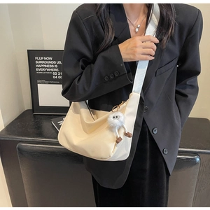 Chic off-white hobo bag with wide fabric strap and plush charm on black suit