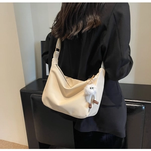 Close-up of cream Hobo bag with wide strap and fuzzy charm accessory in warm indoor setting