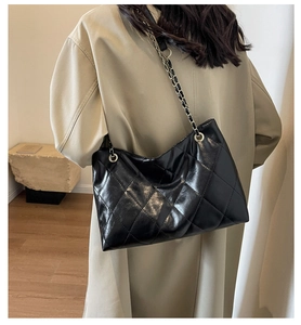 Detail of black glossy quilted leather shoulder bag with silver chain strap on a model