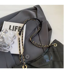 Close-up of black quilted tote bag with gold chain strap on a business blazer