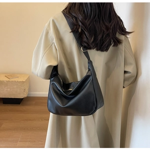 Black pebbled leather hobo bag with wide shoulder strap worn by a model in a beige coat