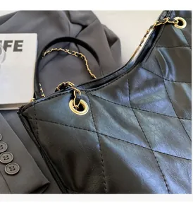 Detailed close-up of glossy black quilted tote bag with golden metal chain strap accents