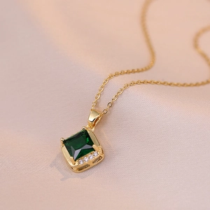 Gold necklace with square green zircon pendant on pink silk background, minimalist style