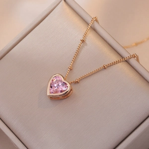 Détail d'un pendentif cœur en zircon rose avec chaîne perlée dorée dans son écrin à bijoux