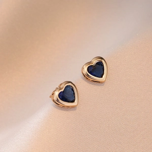 Détail de boucles d'oreilles cœur en zircon bleu plaqué or sur fond de soie beige