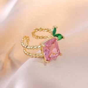 Golden open ring with square pink stone and green leaf accents on pink satin