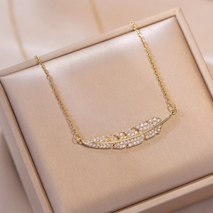 Élégant collier avec pendentif plume dorée et zircons posé sur un écrin à bijoux