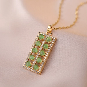 Detail of gold abacus pendant with green gemstones and pavé crystals on silk background