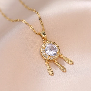 Elegante goldene Traumfänger-Halskette mit Federn und Zirkonia auf Seidenhintergrund