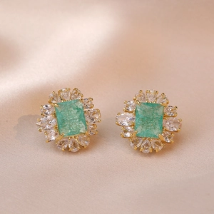 Orecchini vintage con zircone verde smeraldo e petali su sfondo di seta champagne