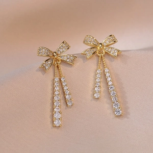 Elegant gold bow earrings with crystal tassels on a luxurious champagne silk background