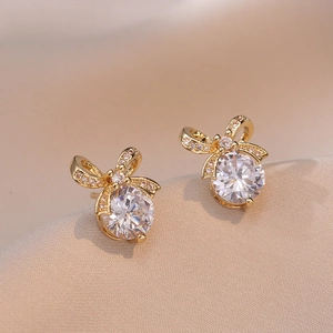 Elegant gold bow earrings with round zircon stones on champagne satin fabric background