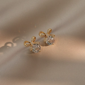 Elegant gold bow earrings with round zircon stones on a luxurious satin fabric background
