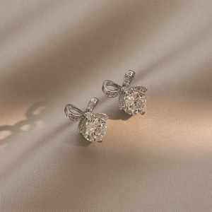 Elegant silver bow earrings with round cubic zirconia on champagne silk background