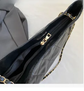 Detail of a smooth golden metal zipper on a black quilted leather shoulder bag