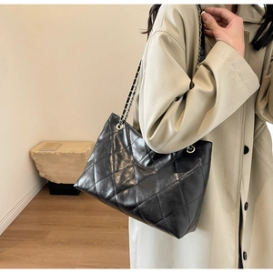 Detail of black quilted tote bag with golden chain strap worn by a model in soft light