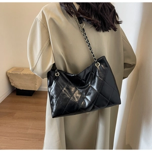 Large black quilted tote bag with golden chain strap on model in trench coat