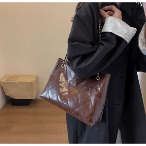 Detail of dark brown quilted tote bag with glossy finish and golden chain strap