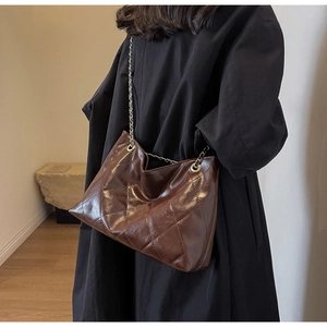 Detail of dark brown quilted tote bag with shiny leather texture and silver chain strap