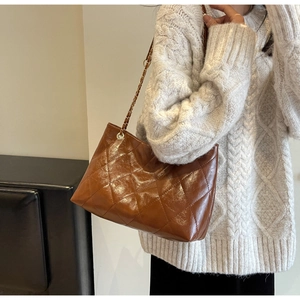 Detail of a brown quilted leather tote bag with chain strap and glossy retro finish