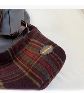 Macro detail of plaid wool fabric texture and leather logo patch on a vintage shoulder bag