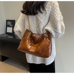 Brown quilted tote bag with gold chain strap shown on a white tweed sweater for women