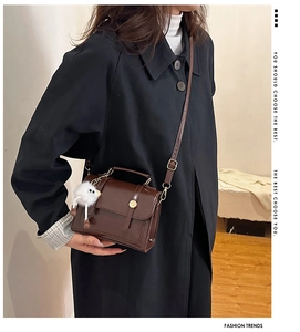 Détail d'un sac bandoulière vintage marron en PU avec boucle dorée et pompon blanc décoratif
