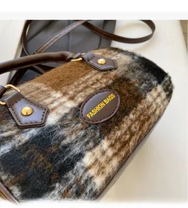 Detail of winter plaid plush handbag with brown leather handles and golden rivets