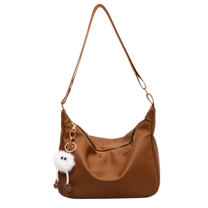 Brown soft PU leather hobo bag with wide strap and white plush charm on white background