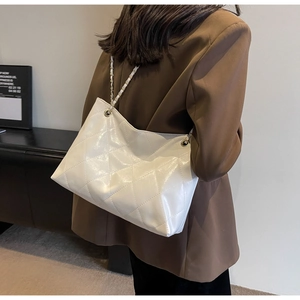 Woman in brown blazer wearing a white quilted shoulder bag with gold chain strap