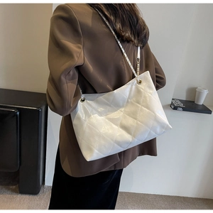 Detail of white quilted tote bag featuring metallic chain strap on a blazer outfit