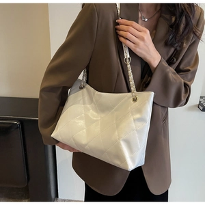 White quilted faux leather tote bag with gold chain strap worn by a woman in a brown blazer