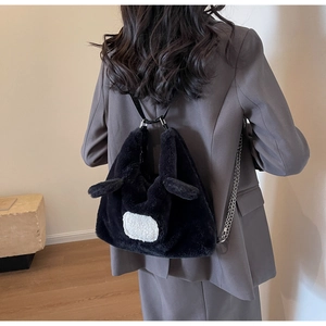 Black plush rabbit backpack with ears and metal chain straps on modern grey suit model