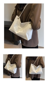 Macro detail of white quilted faux leather tote bag with metal chain strap on model