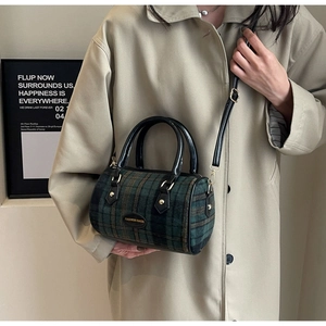 Detail of green and black plaid barrel bag featuring leather handles and golden hardware
